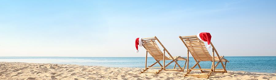 Sun loungers with Santa\'s hats on beach, banner design. Christmas vacation